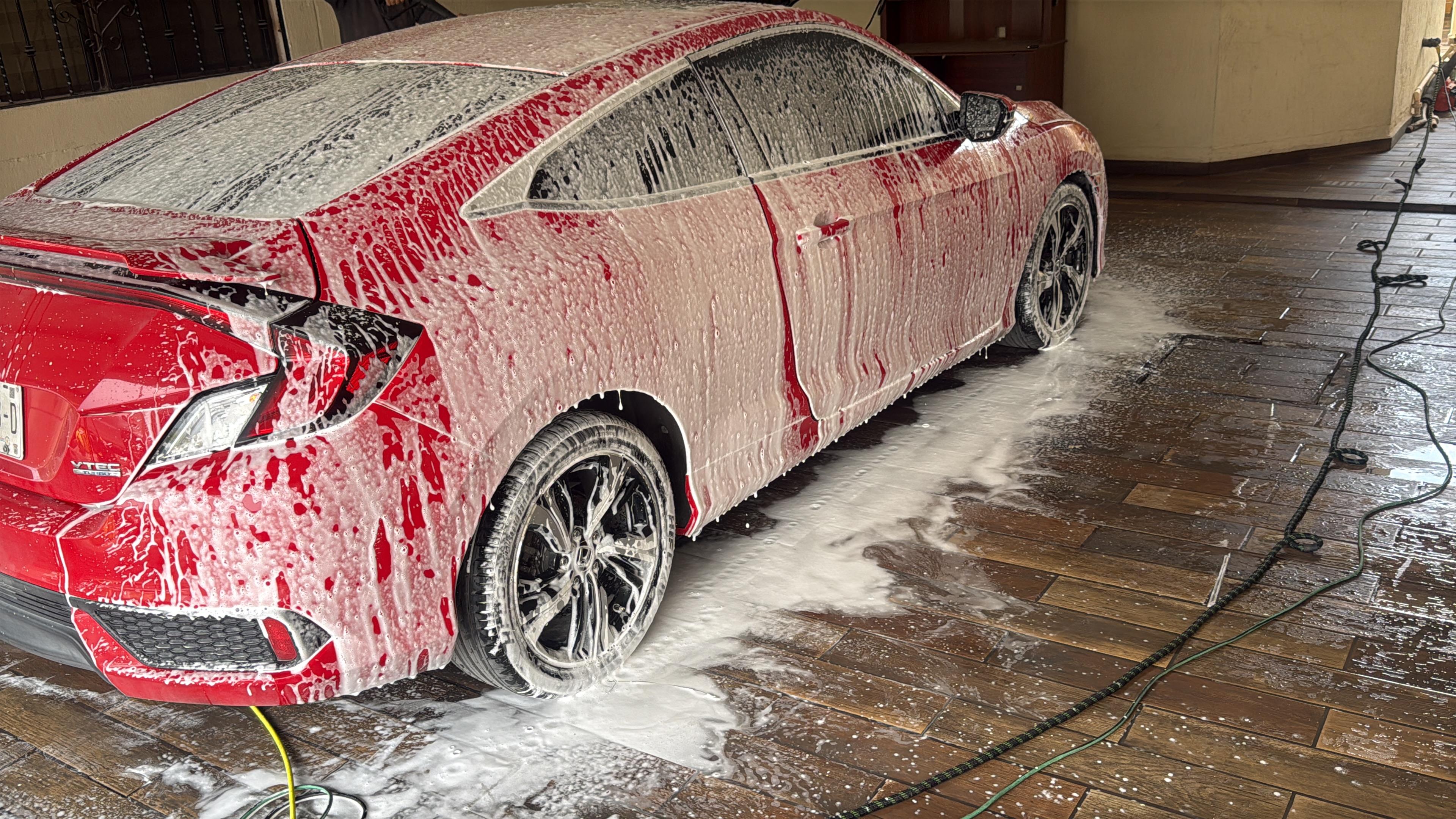 Automóvil rojo cubierto de espuma blanca durante el proceso de lavado.